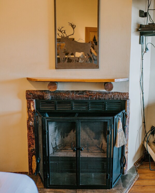 A fireplace with a decorative mirror above it, a mantel with a deer silhouette, and a log fire inside. - Bar N Ranch (West Yellowstone)