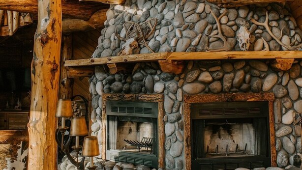 Un interior rústico con chimenea de piedra, vigas de madera y una rama de ciervo decorativa.