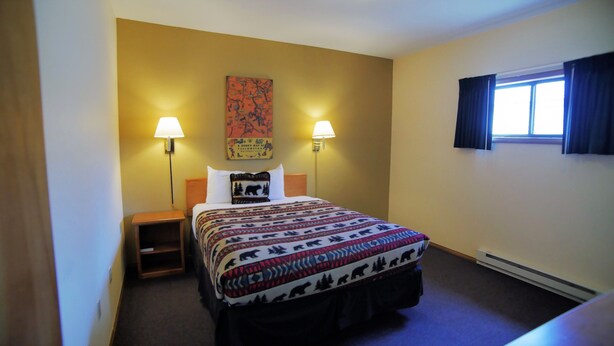A hotel room with a bed, two bedside lamps, a map on the wall, and a window with curtains. - City Center Motel (West Yellowstone)