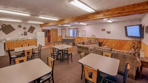 A spacious room with wooden beams, a kitchen area, and a seating area with tables and chairs. - City Center Motel (West Yellowstone)
