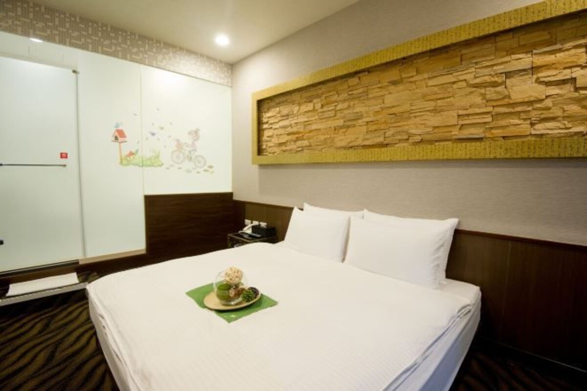 A hotel room with a neatly made bed, a stone accent wall, a wooden headboard, and a white wardrobe.