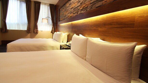 A hotel room with two beds, a stone accent wall, and a nightstand with a lamp.