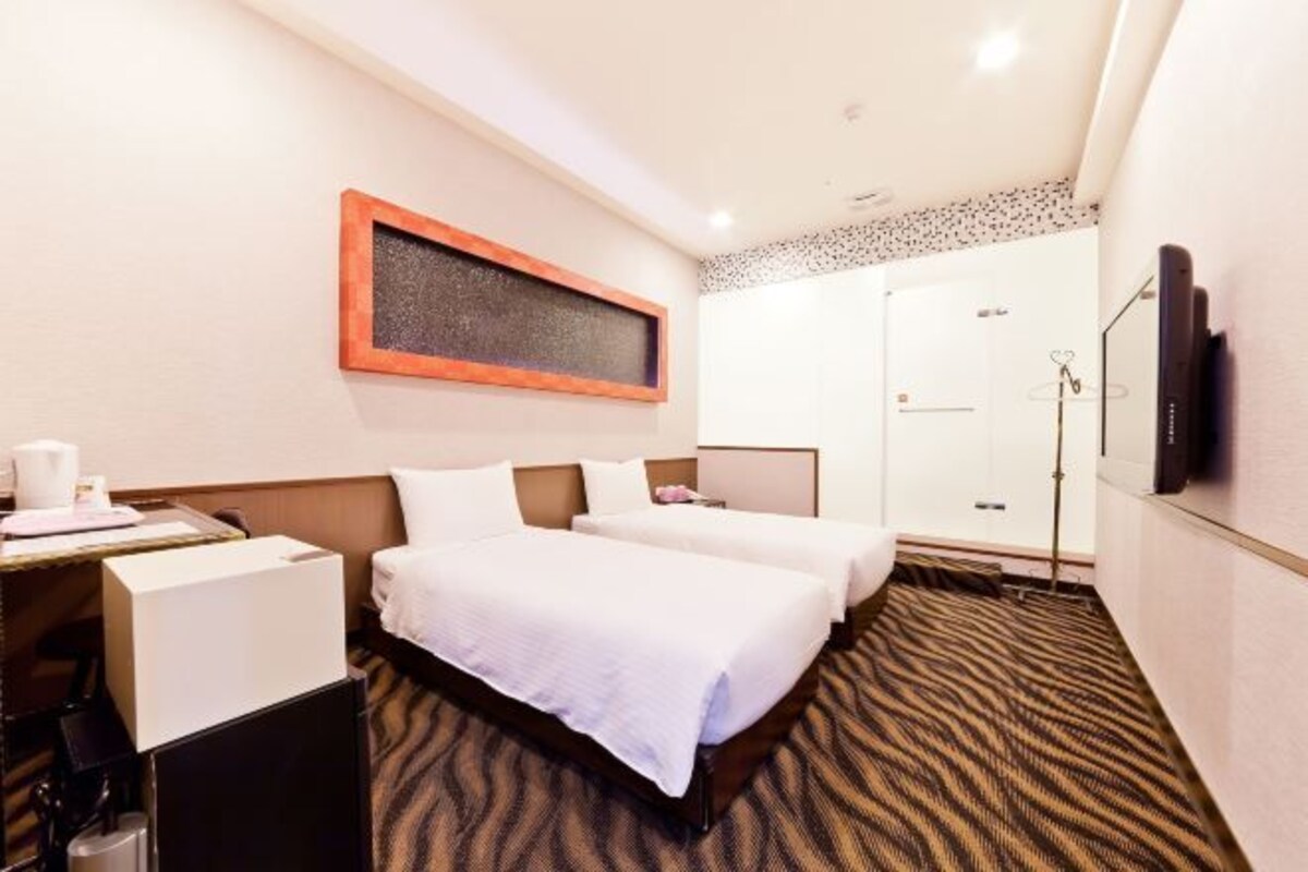 A hotel room with two beds, a desk, a coffee machine, a shower, and a TV.