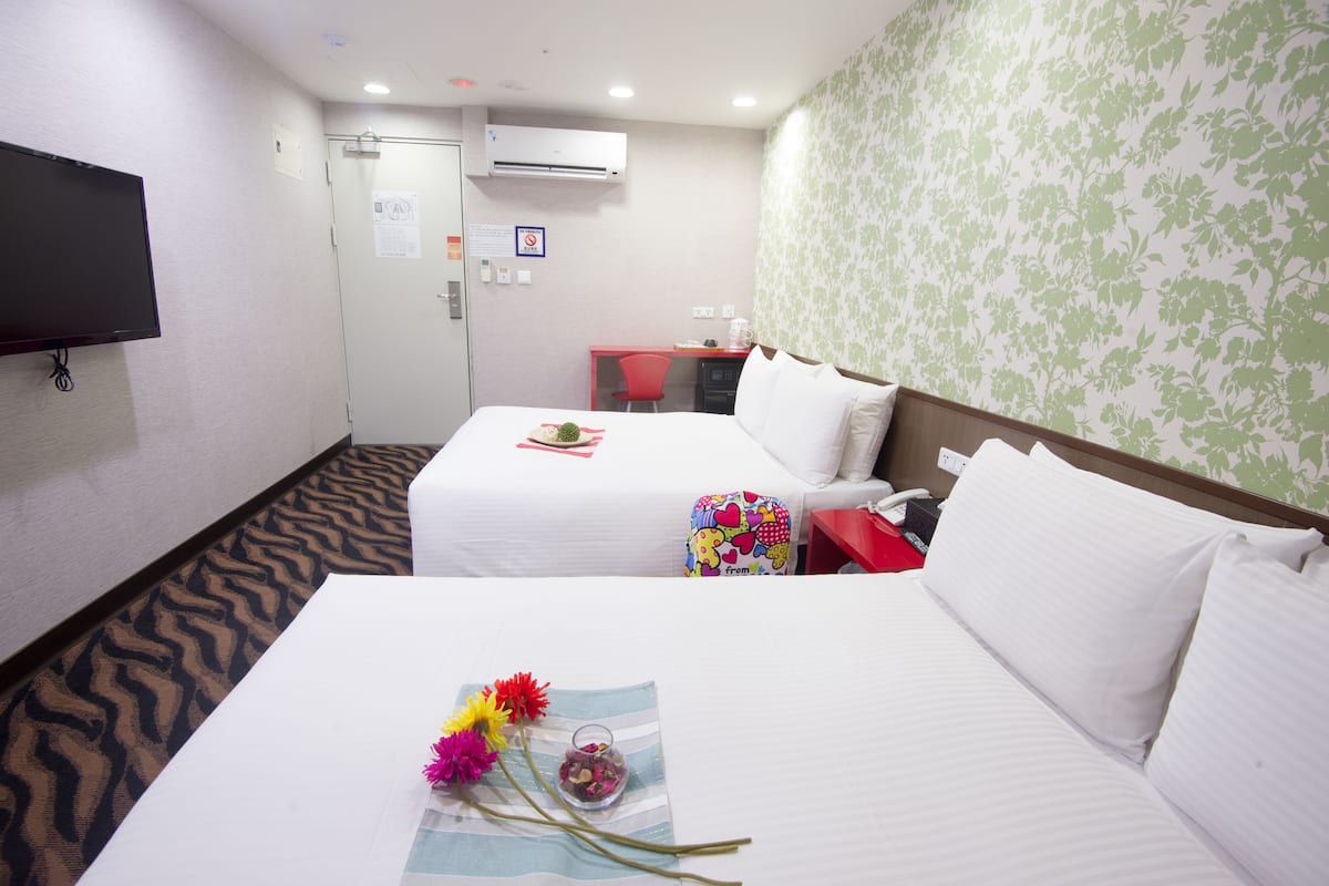 A hotel room with two beds, a TV, an air conditioner, a desk, and a red chair.