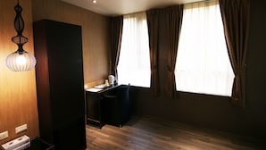 A room with a wooden floor, a desk with a chair, a hanging light fixture, and a window with curtains.