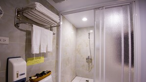 Une salle de bain avec une douche à parois de verre, des toilettes équipées d’un distributeur d’essuie-tout et un porte-serviettes avec des serviettes pliées.