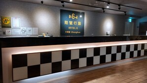 Un comptoir d’accueil d’hôtel au design à carreaux noirs et blancs, une enseigne indiquant le nom de l’hôtel en chinois, et diverses cartes d’information.