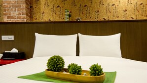 Une chambre d’hôtel avec un lit bien fait, une petite table de chevet sur laquelle se trouve une boîte de mouchoirs, et un plateau décoratif avec de petites plantes.