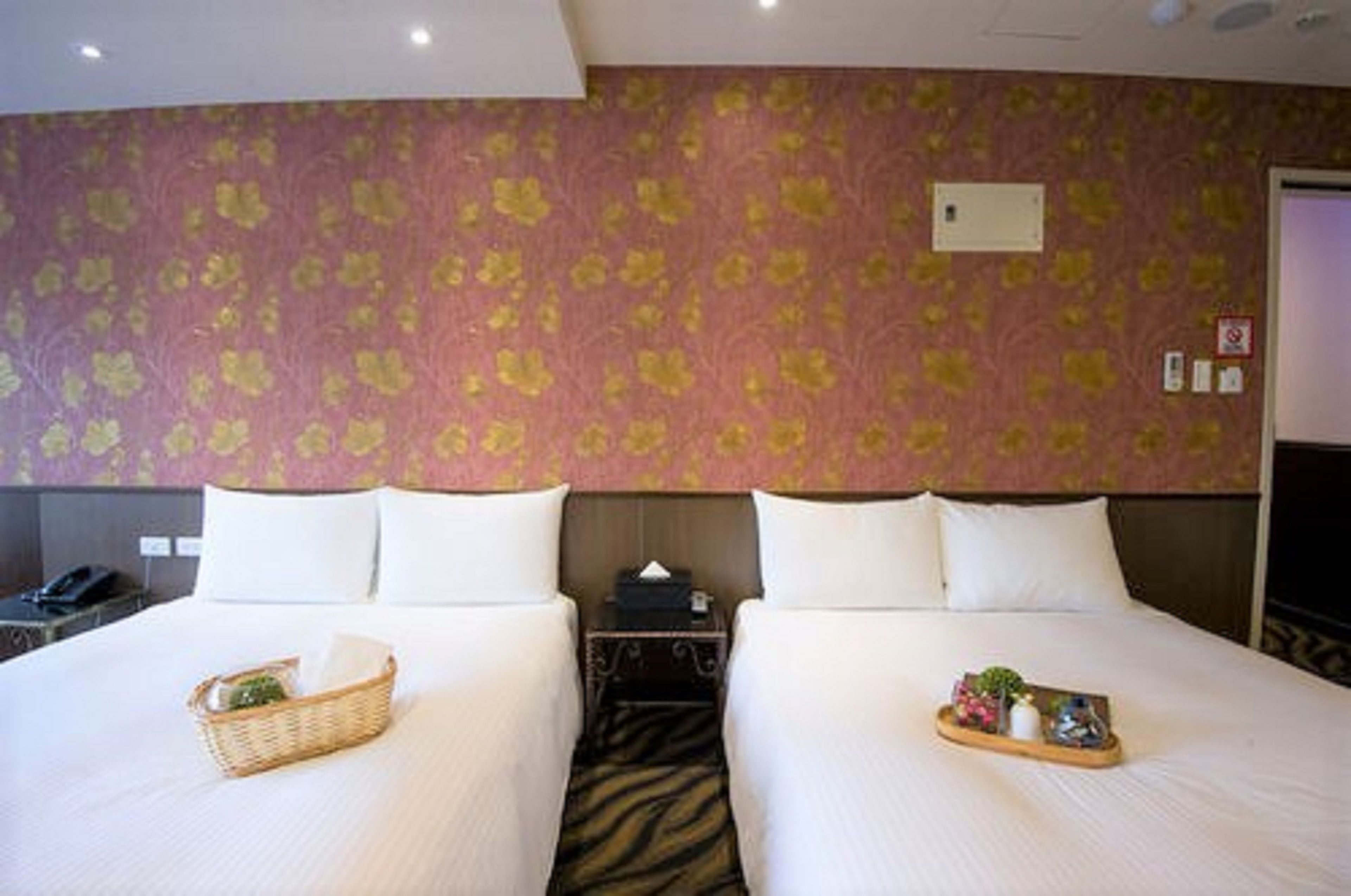 A hotel room with two beds, a patterned wallpaper, a nightstand, and a tray with items on the bed.