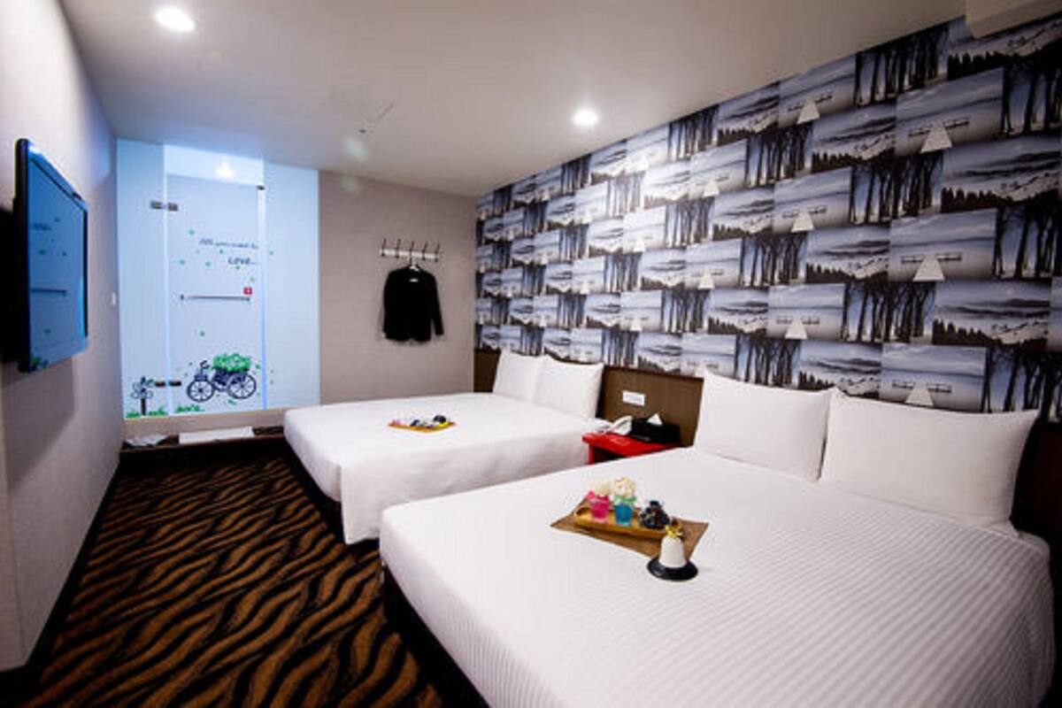 A hotel room with two beds, a large window with a view, a wall with a patterned design, and a mounted television.