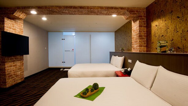 Une chambre d’hôtel avec deux lits, un mur en briques, un téléviseur à écran plat et une porte donnant accès à une salle de bain.