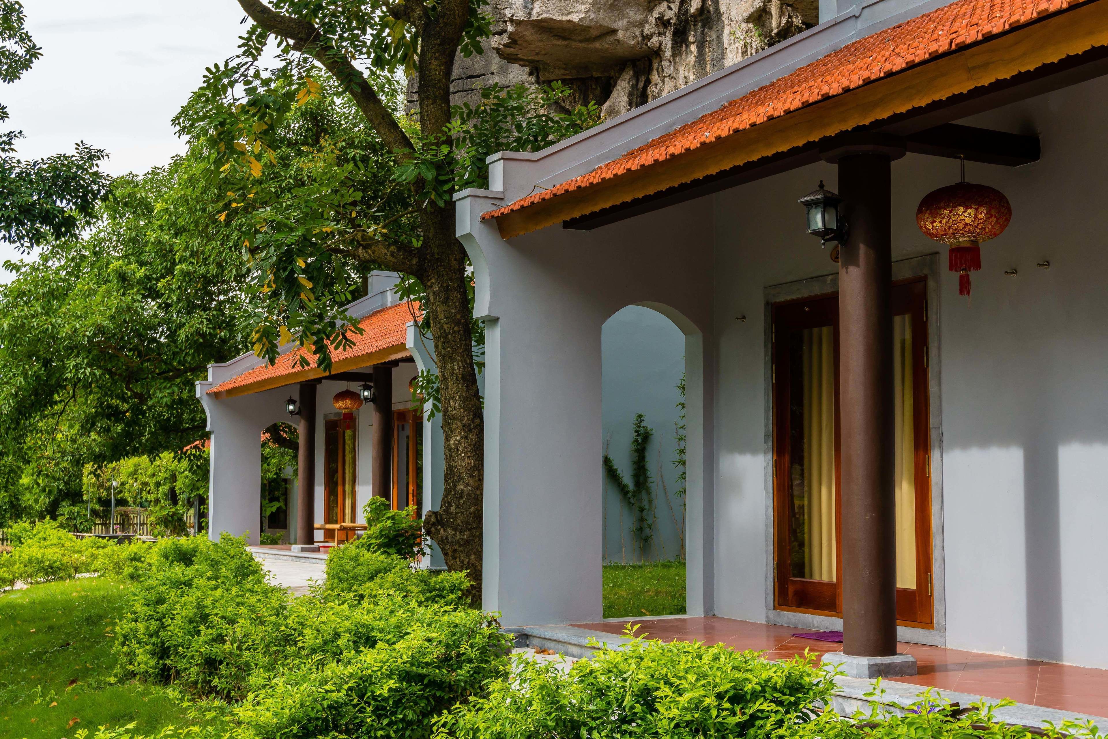 A traditional building with a tiled roof, wooden columns, and a garden area with green shrubs.