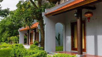 A traditional building with a tiled roof, wooden columns, and a garden area with green shrubs.