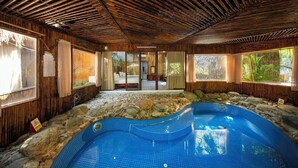 A spa area with a hot tub surrounded by stone, wooden walls, and large windows. - Mua Caves Ecolodge (Hoa Lu)