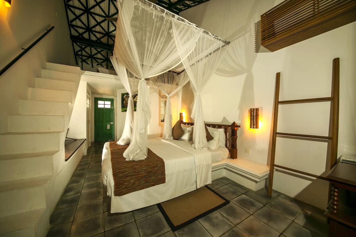 A bedroom with a bed under a canopy, a staircase, and a wooden bench.