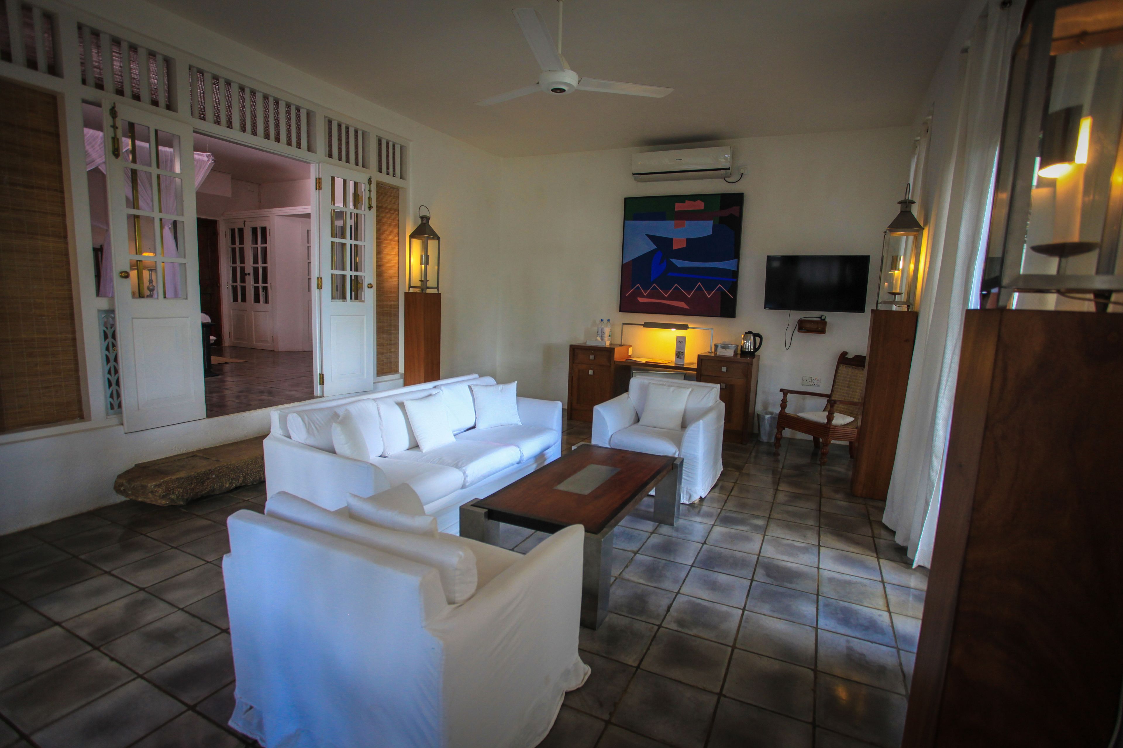 A spacious living area with a white sofa set, a wooden coffee table, and a television mounted on the wall.