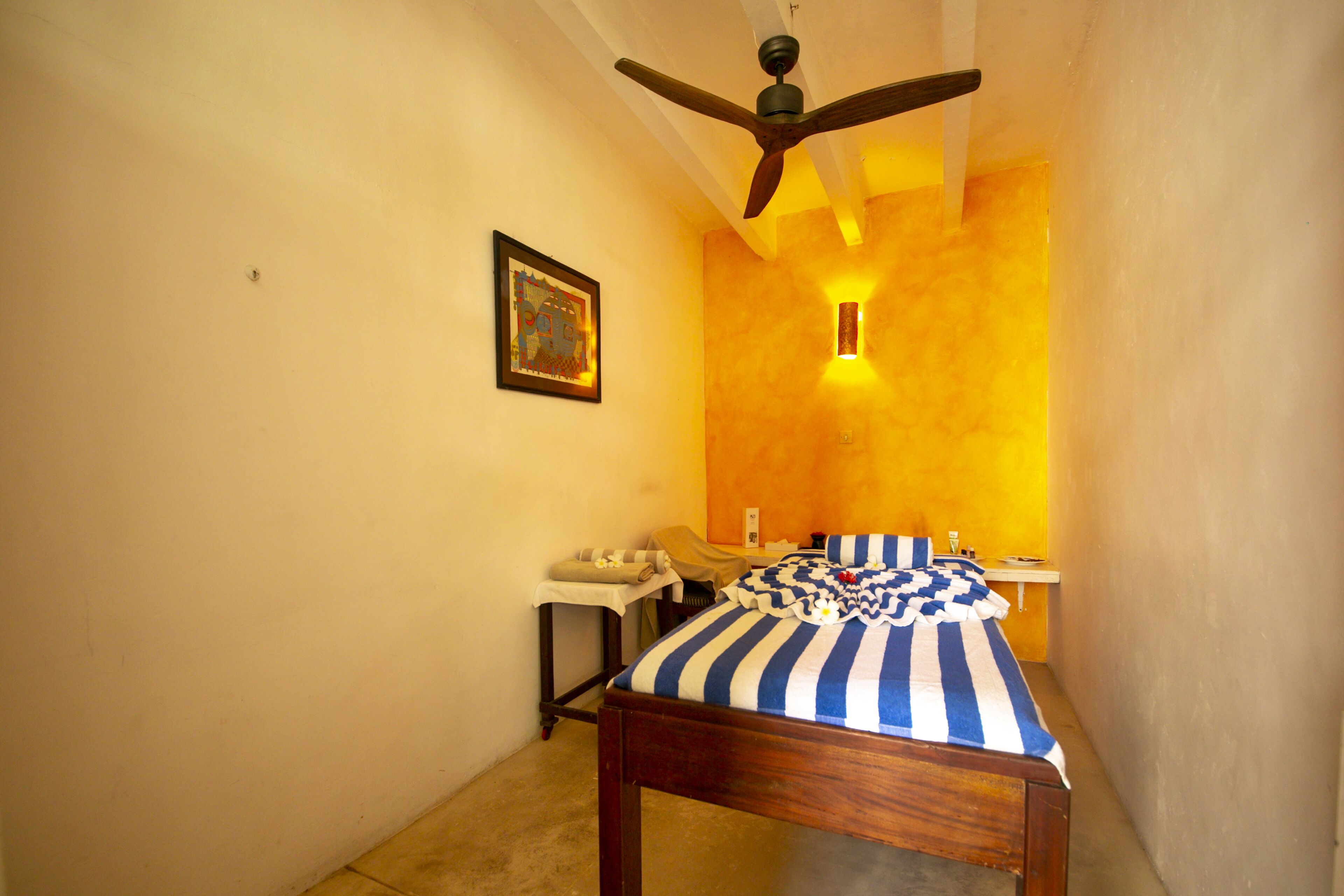 A small, narrow room with a single bed, a nightstand, and a ceiling fan.