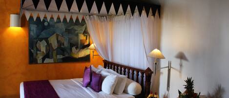 A hotel room with a bed, a nightstand, a lamp, a fruit bowl, and a painting on the wall.