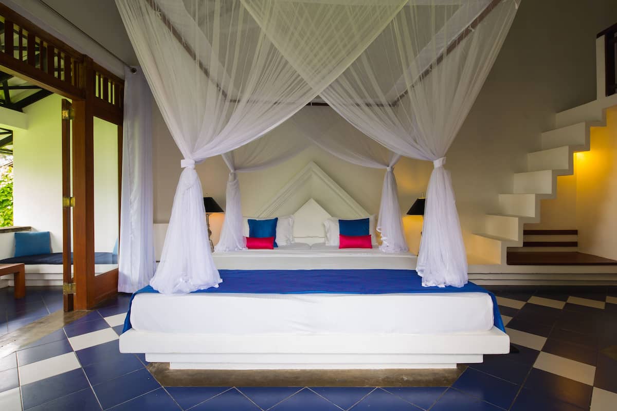 A bedroom with a bed under a canopy, a staircase, and a checkered floor.