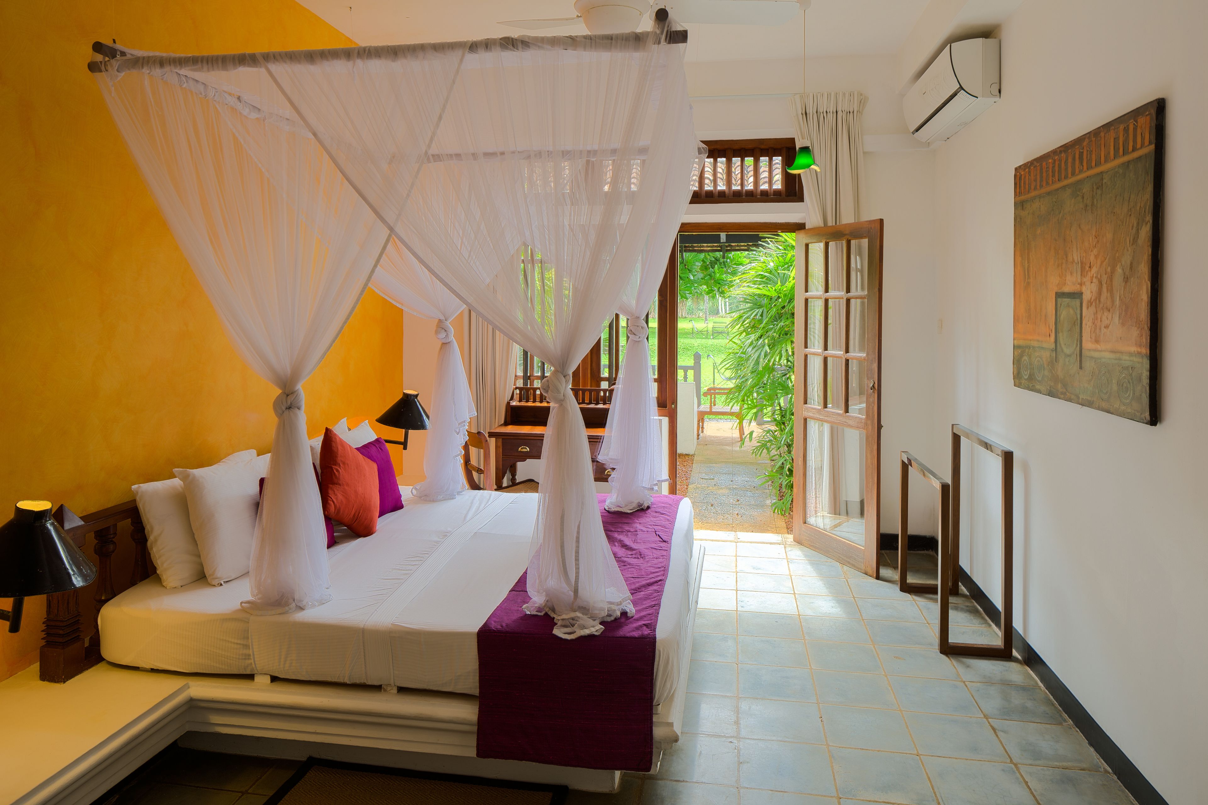 A bedroom with a bed, a nightstand, a lamp, a window with curtains, and a door leading to a balcony.