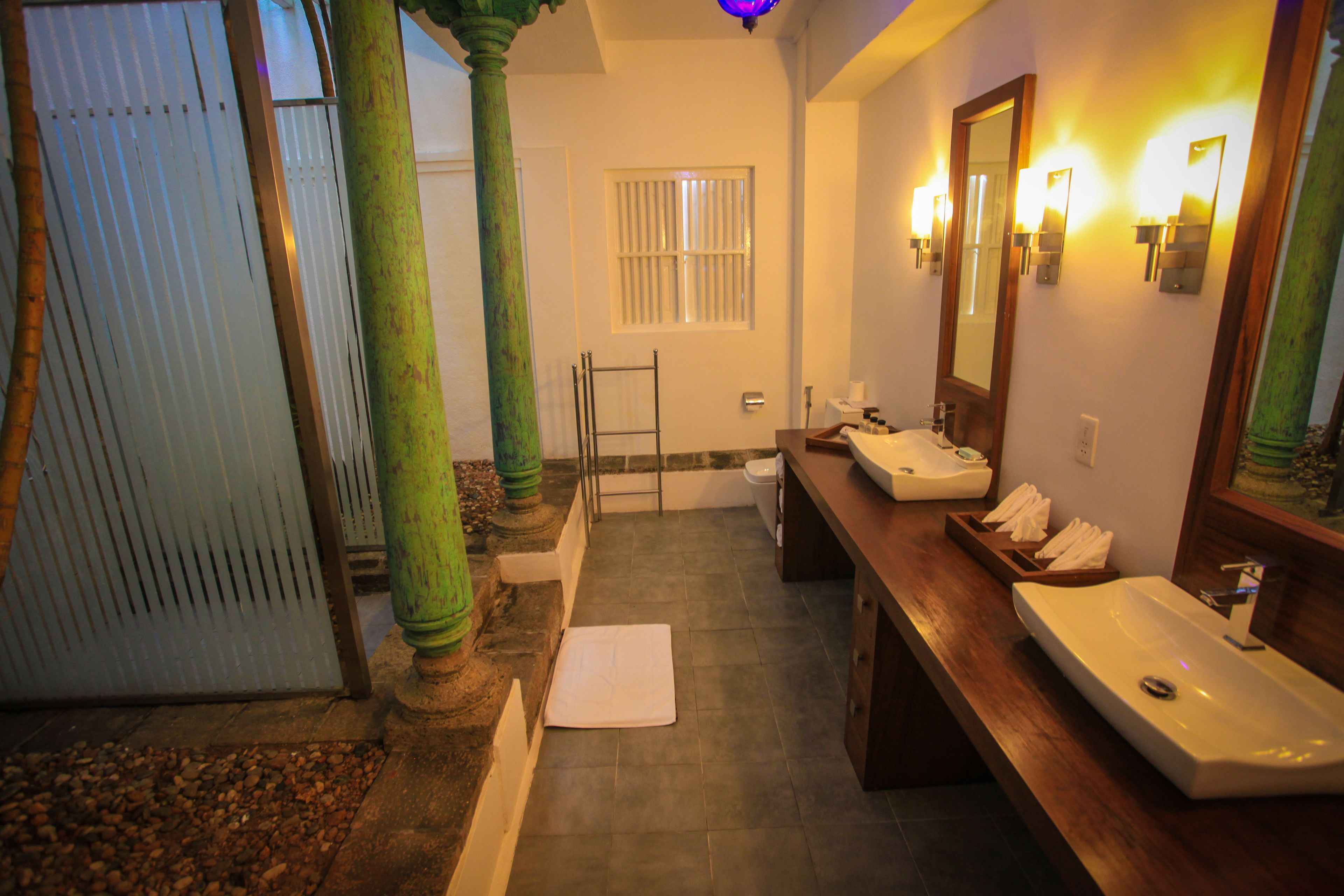Ein Badezimmer mit Badewanne, Waschbecken und Spiegel. Auf dem Boden liegt ein Handtuch und eine Holzbank steht daneben.
