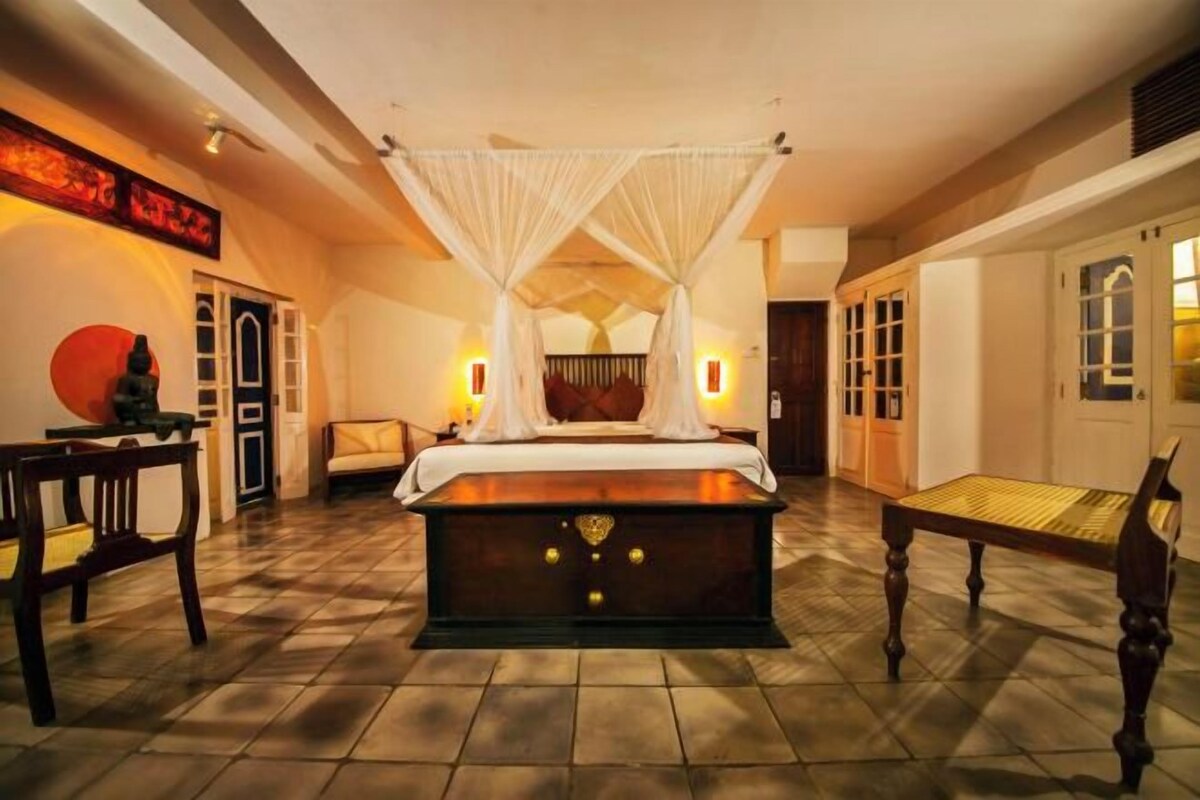 A spacious bedroom with a large bed, a bedside table, a chair, and a small table.