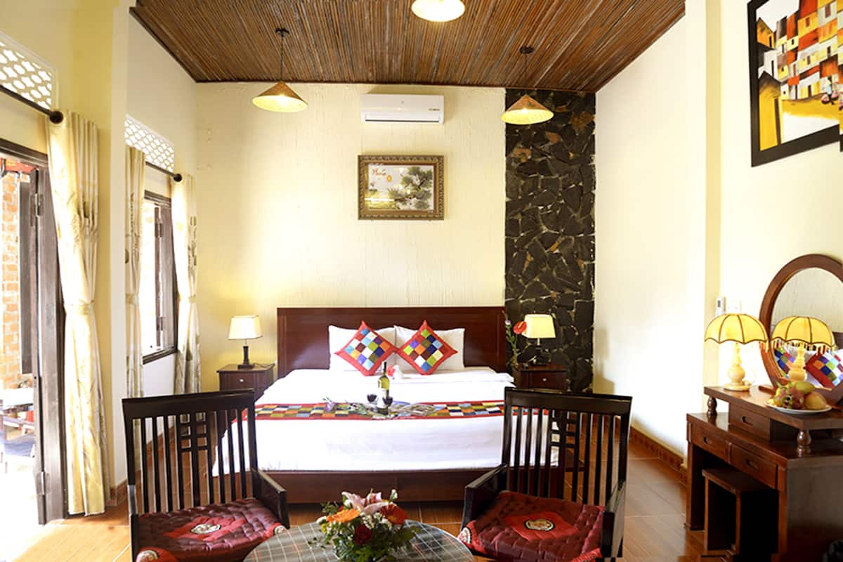 A hotel room with a bed, two chairs, a table with a vase, a mirror, and a picture on the wall.