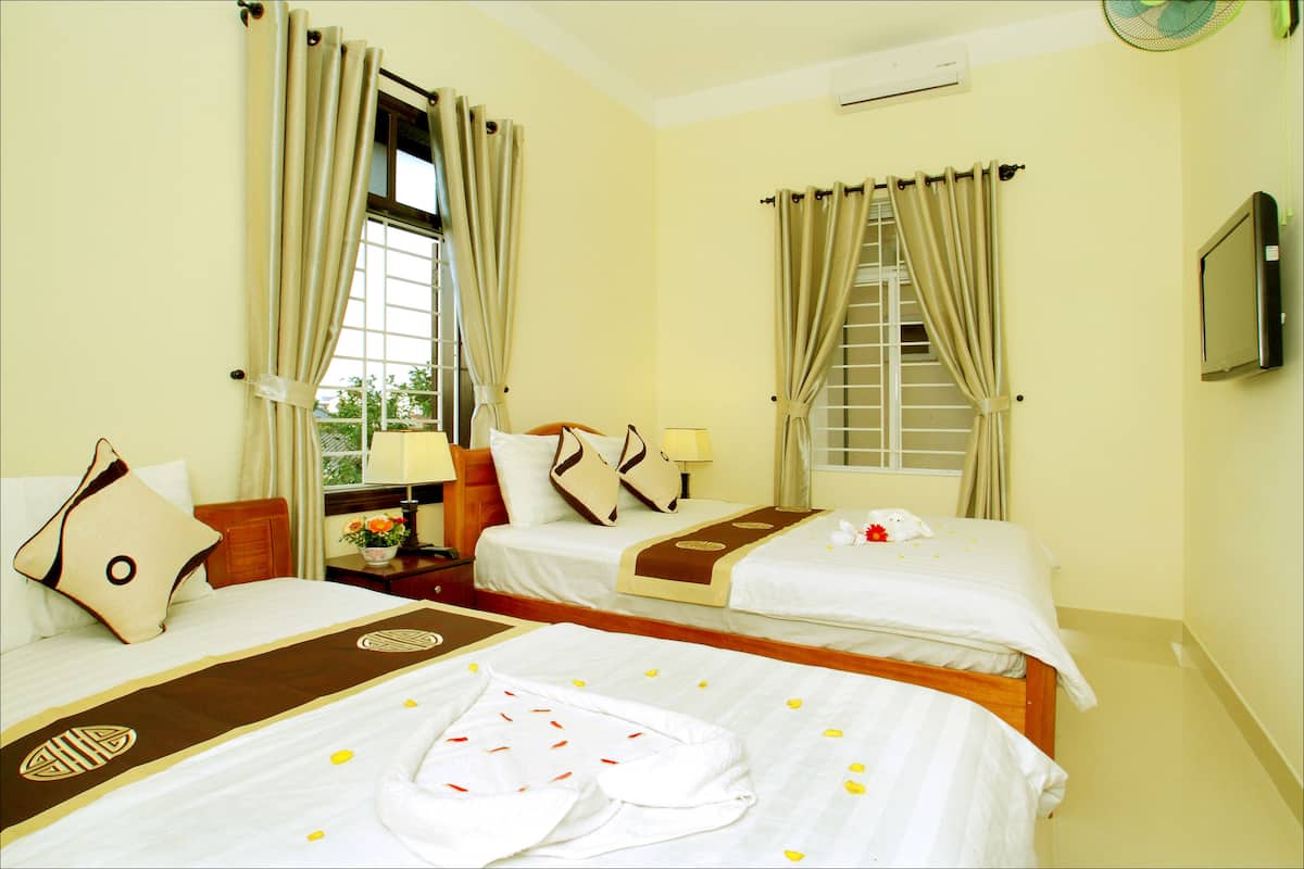 A hotel room with two beds, a window, a fan, and a TV.