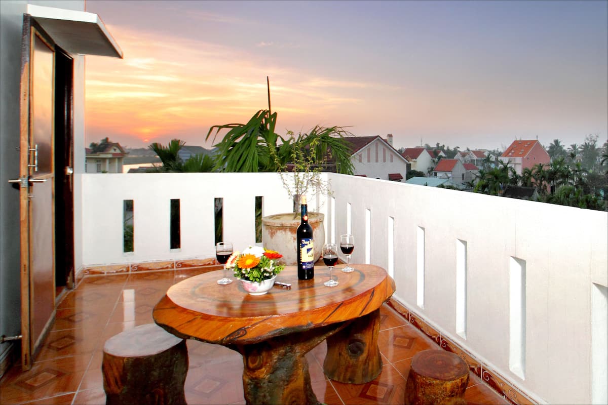 A round wooden table with a bottle and glasses on a balcony with a sunset view.