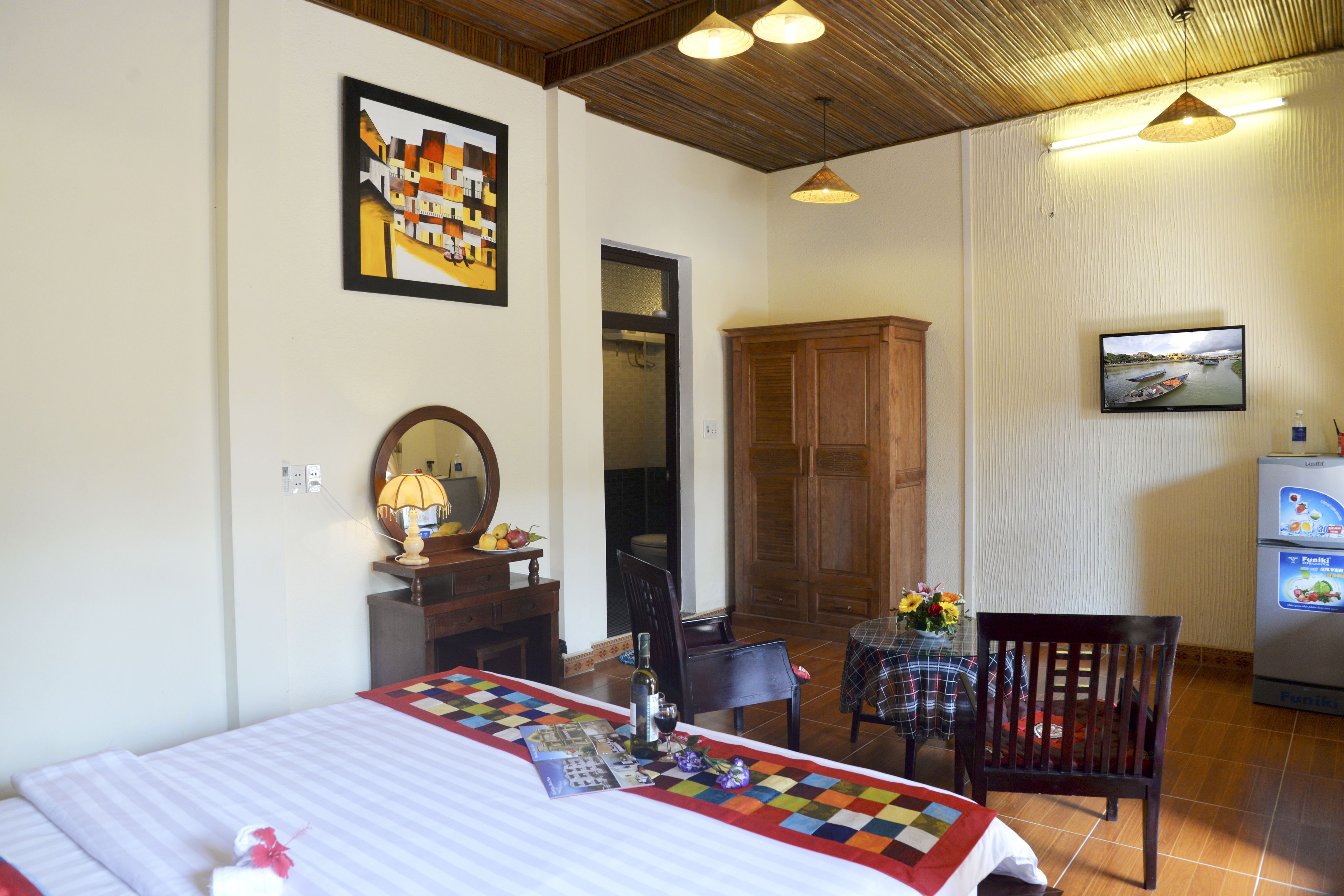 A hotel room with a bed, a dining table with chairs, a television, and a refrigerator.