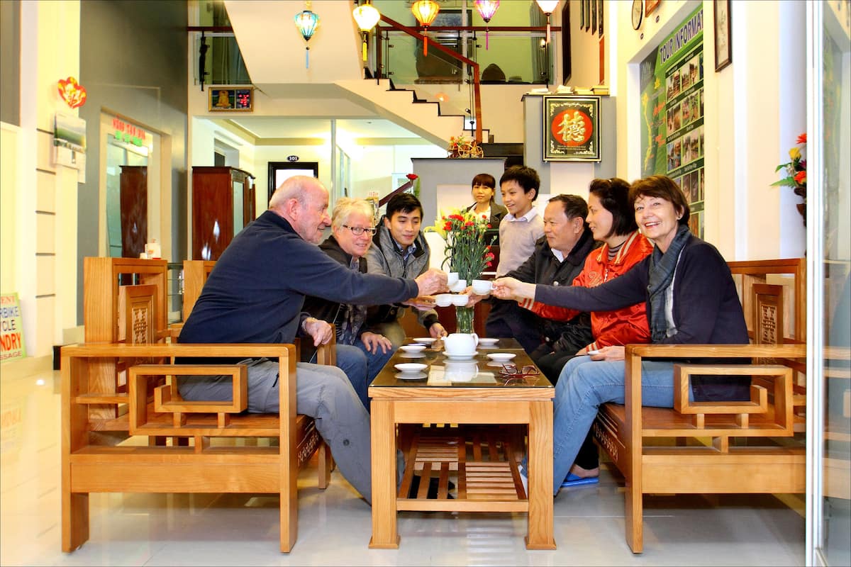 A group of people seated around a table in a well-lit indoor space with wooden furniture and a staircase in the background.