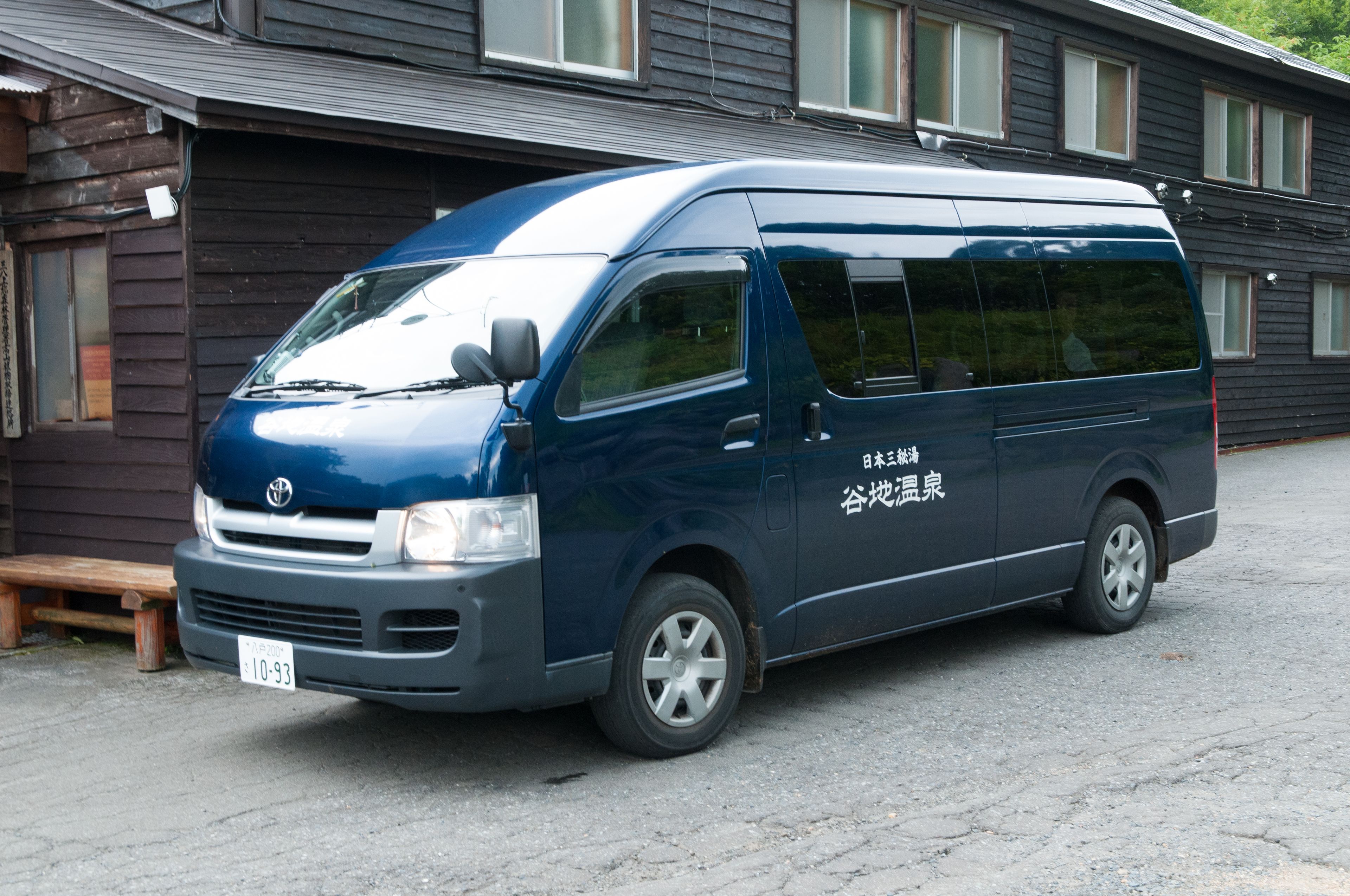 A blue van parked in front of a building with Japanese text on the side.