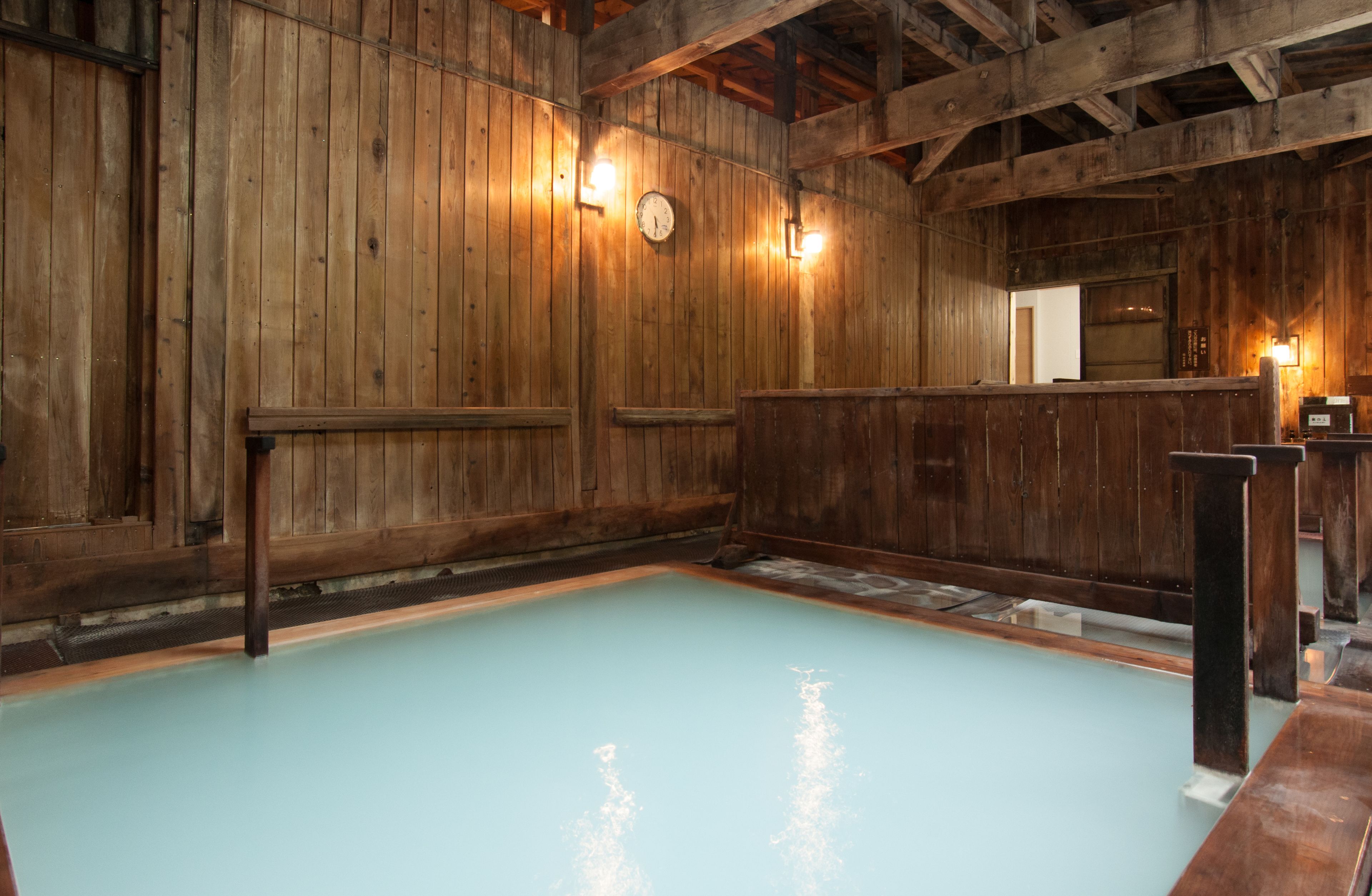 A wooden interior with a pool, wooden benches, and a clock on the wall.