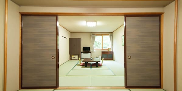 Una habitación japonesa tradicional con suelo de tatami, puertas correderas, un televisor y una pequeña mesa con sillas.