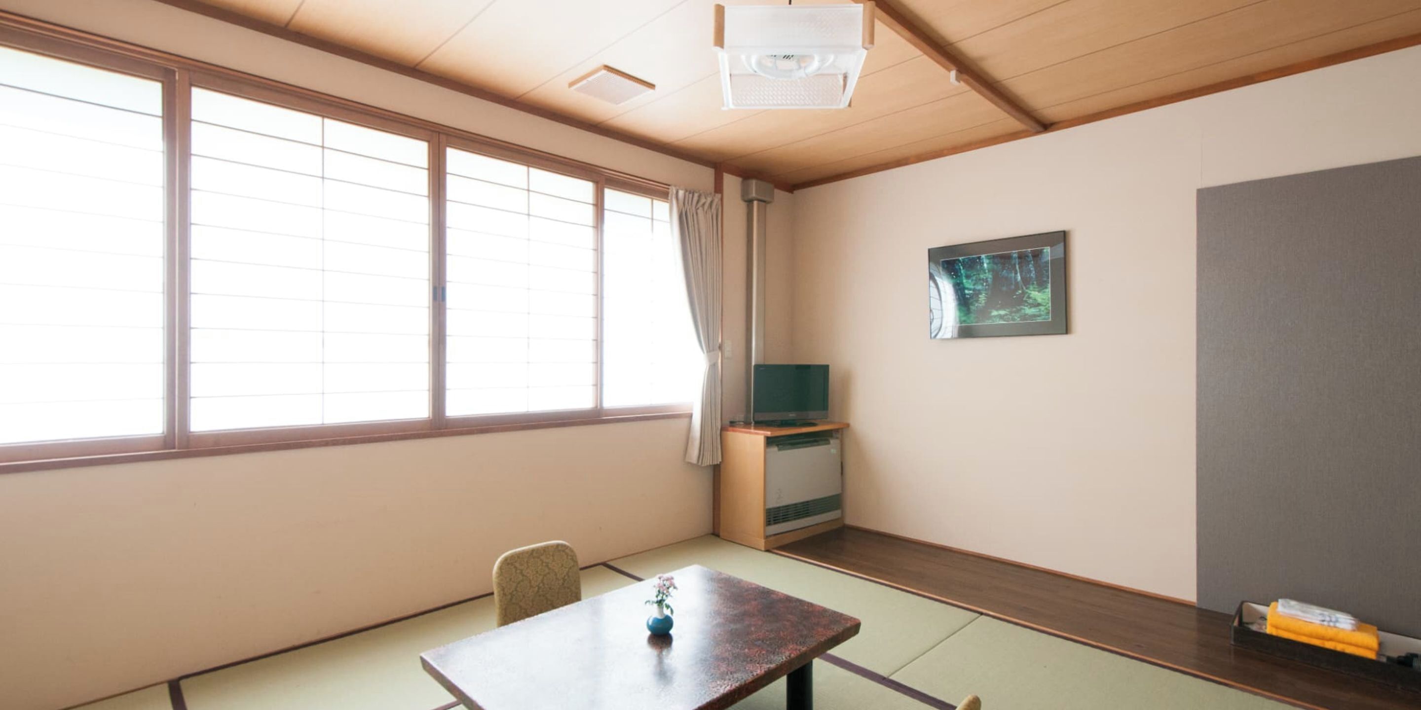A room with a wooden table, a chair, a television on a stand, and a framed picture on the wall.