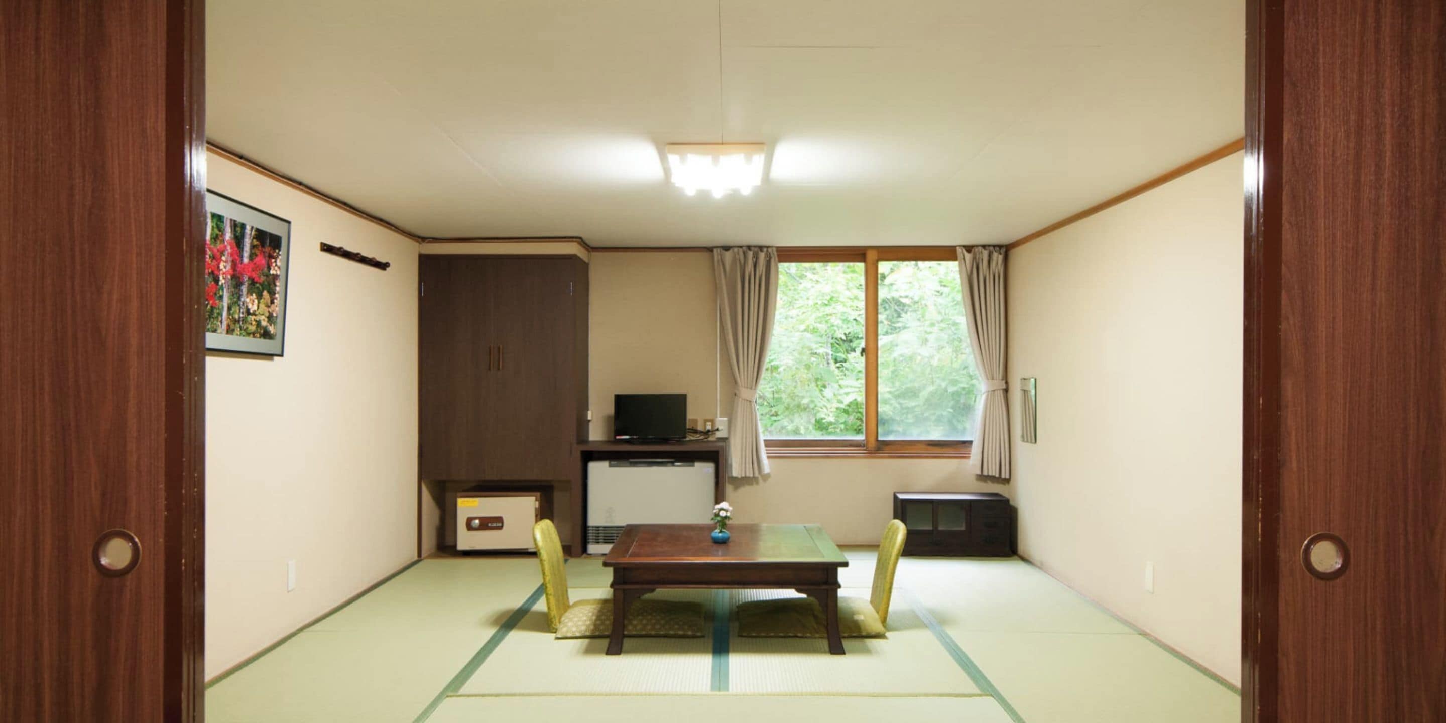 Una habitación japonesa tradicional con suelo de tatami, una mesa de madera, un televisor y un armario.