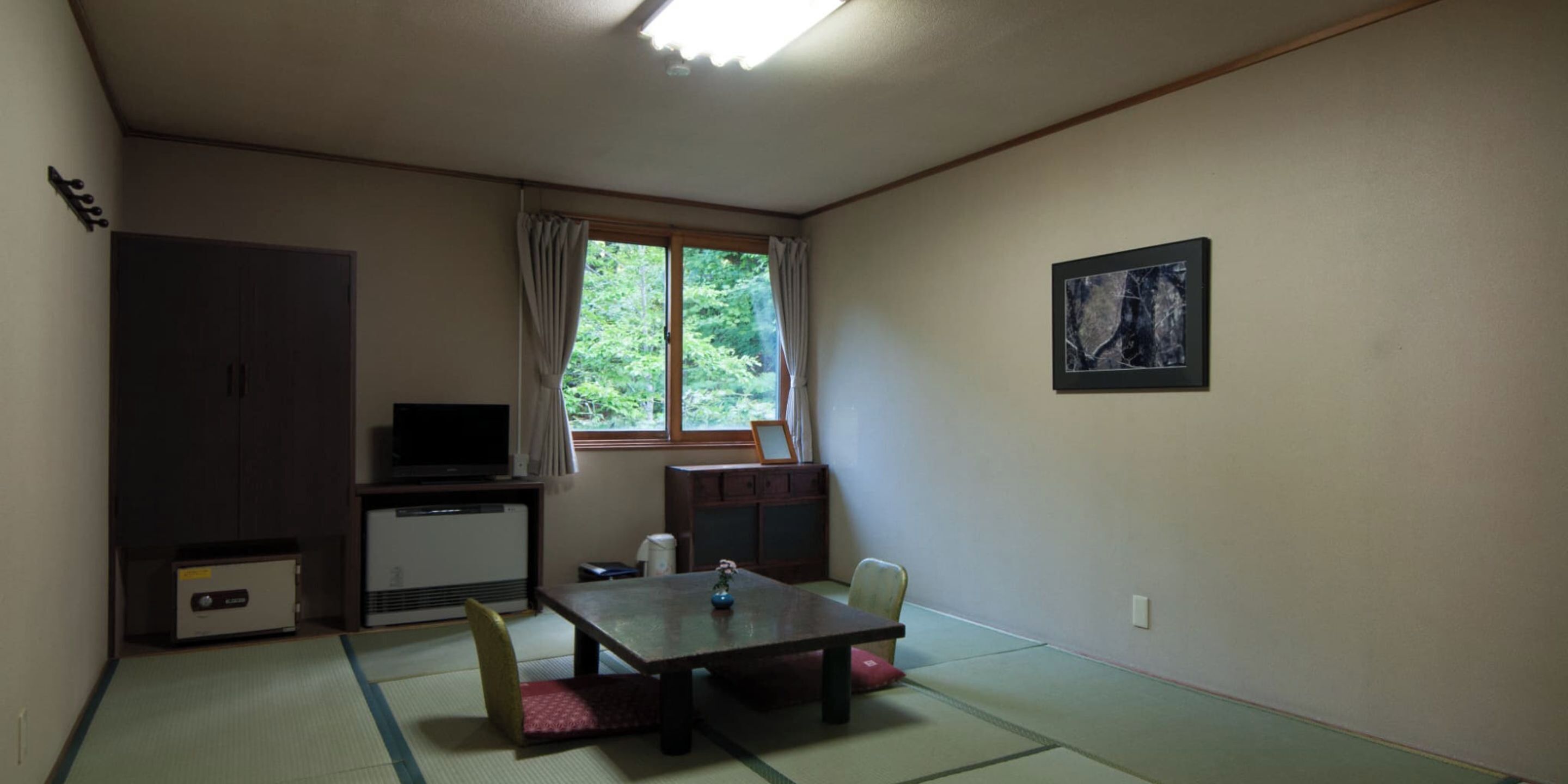 Habitación con suelo de tatami, una mesa baja, televisor, armario y ventana con cortinas.