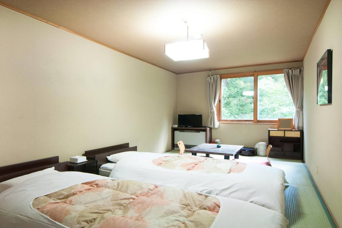 Una habitación de hotel con dos camas, televisión, escritorio y ventana con cortinas.