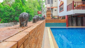 A swimming pool adjacent to a brick wall with a row of elephant statues.