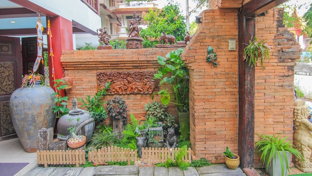 A traditional Thai courtyard with a brick wall, a wooden fence, and various statues and plants.