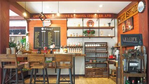 A coffee shop interior with wooden furniture, a menu board, and shelves with coffee and tea products.
