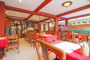 A restaurant with wooden tables and chairs, red tablecloths, and a brick wall with hanging plants.