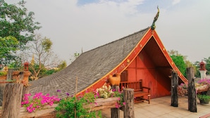 A traditional Thai house with a sloped roof, wooden porch, and a bench.