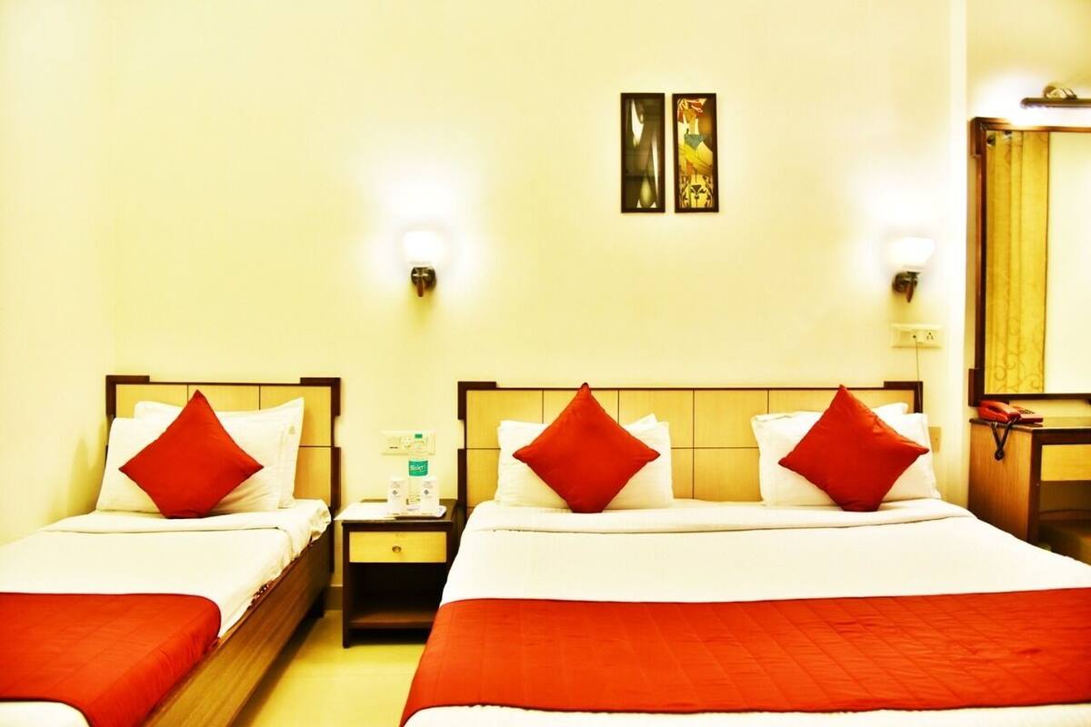 A hotel room with two beds, each with red pillows and a red blanket. There are wall-mounted light fixtures and a small table with a bottle of water.