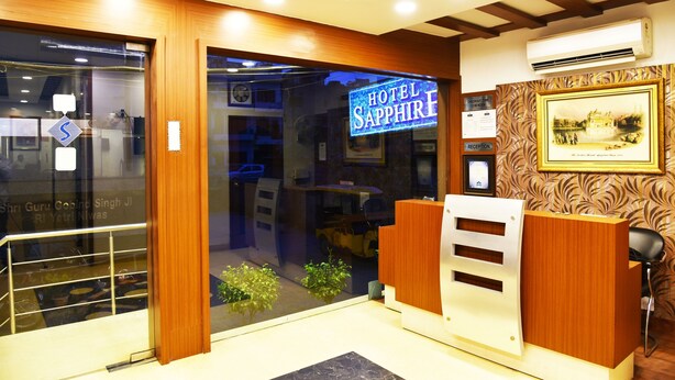 A hotel reception area with a neon sign, reception desk, and framed artwork on the wall. - Hotel Sapphire (Amritsar)