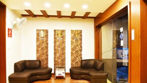 A reception area with two brown leather sofas, a standing fan, and a glass partition with a view. - Hotel Sapphire (Amritsar)