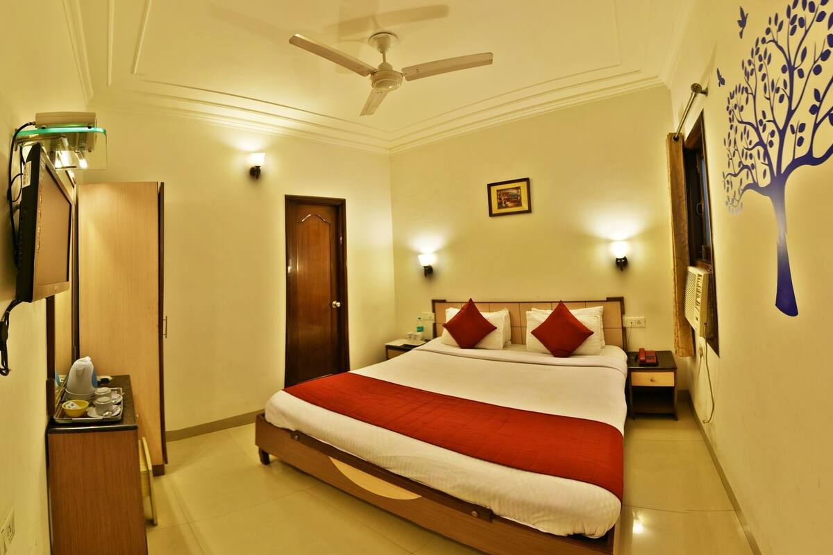 A hotel room with a bed, bedside table, nightstand, wall-mounted lamp, ceiling fan, and a door.