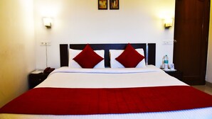 A hotel room with a large bed, red and white bedding, two wall-mounted light fixtures, and a door. - Hotel Sapphire (Amritsar)