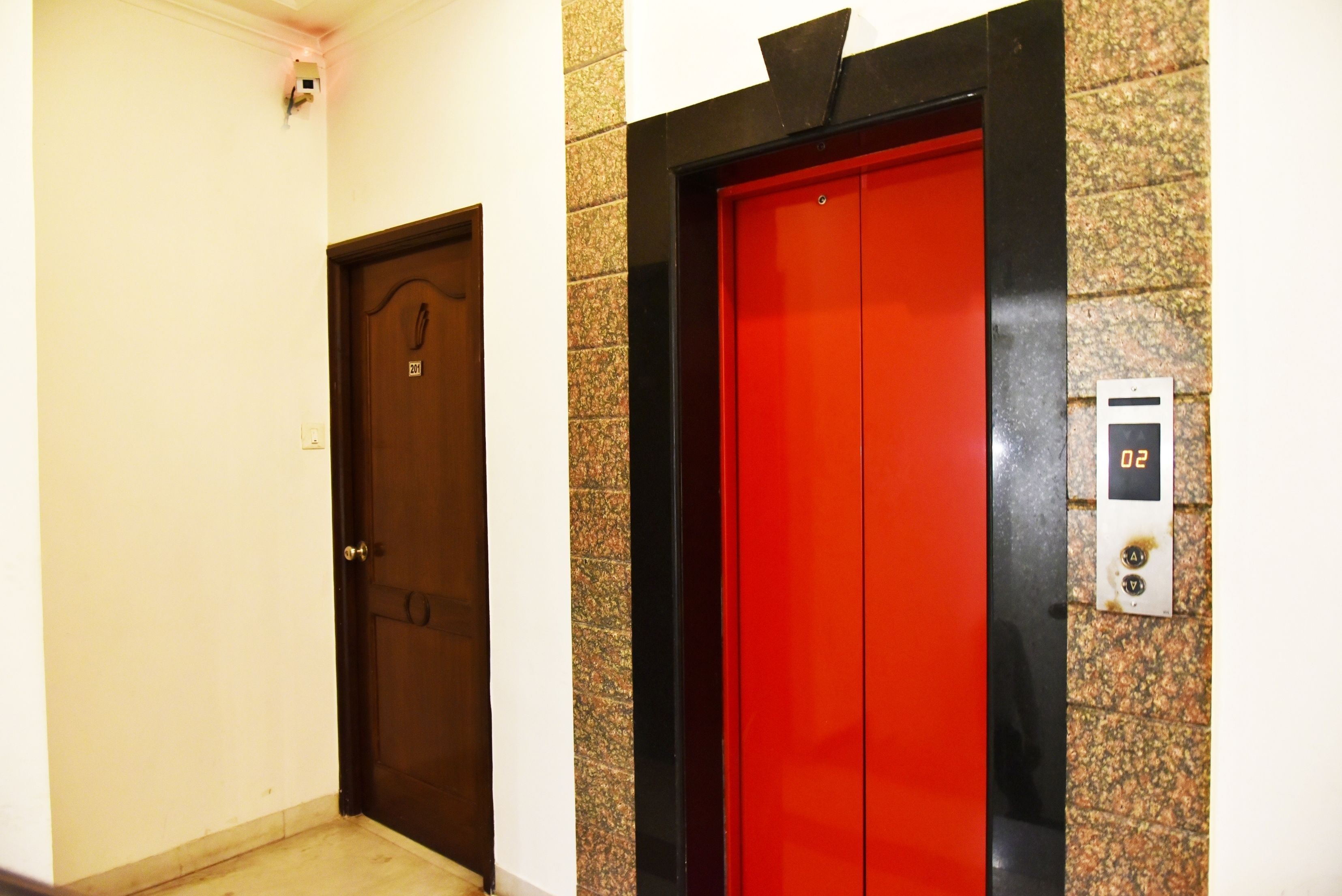 A hallway with a wooden door and a red elevator door with a digital display.