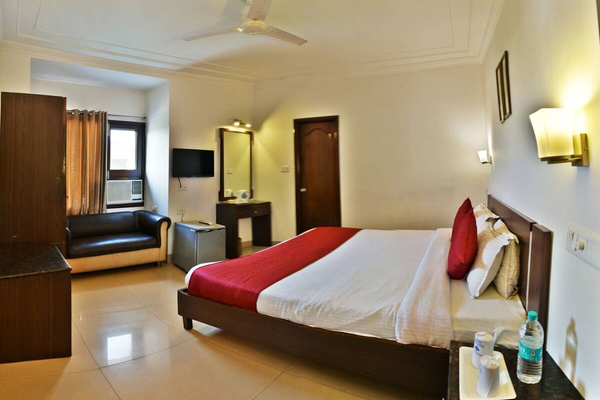 A hotel room with a bed, a desk, a chair, a TV, a mirror, and a ceiling fan.